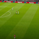 An expansive view of a lush green football pitch at the San Siro Stadium, capturing the atmosphere of an intense Serie A clash between AC Milan and Parma.