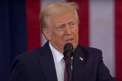 Donald Trump speaking at a public event, addressing an audience with a serious expression.