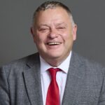 Mike Amesbury, a well-known British politician and Labour Party MP, photographed in a professional setting wearing a gray suit and red tie.