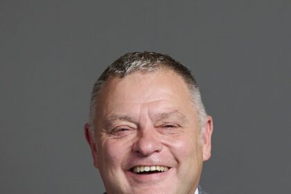 Mike Amesbury, a well-known British politician and Labour Party MP, photographed in a professional setting wearing a gray suit and red tie.