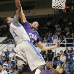 Basketball player jumping mid-air to score during an intense game with a cheering crowd in the background.