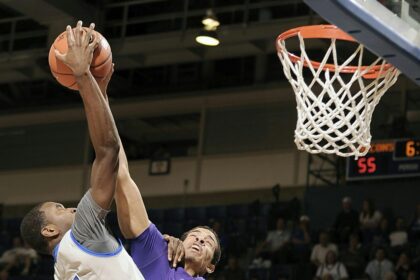 Basketball player jumping mid-air to score during an intense game with a cheering crowd in the background.