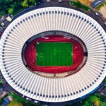 Aerial view of a stadium showcasing its vibrant green pitch surrounded by seating areas, symbolizing the grandeur of sporting events.