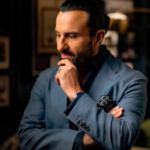 A professional portrait of Bollywood actor Saif Ali Khan, featuring him in a thoughtful pose, wearing a formal blue suit. The image is sourced from the official Instagram handle of Saif Ali Khan.