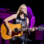 A live performance of Sheryl Crow playing the guitar on stage.