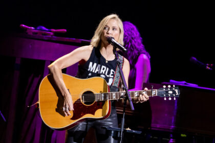 A live performance of Sheryl Crow playing the guitar on stage.