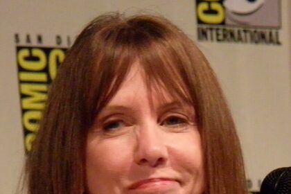 Laraine Newman at a public event, speaking into a microphone and smiling.