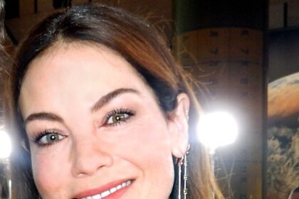 Michelle Monaghan attending a red carpet event, smiling in a beige dress with elegant makeup.