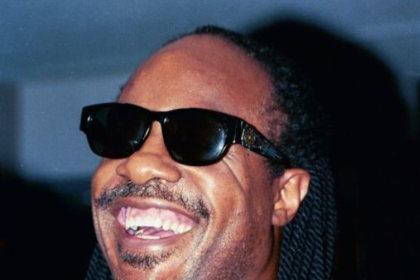 Stevie Wonder performing at an event, wearing his signature sunglasses and a stylish outfit.