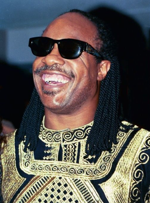 Stevie Wonder performing at an event, wearing his signature sunglasses and a stylish outfit.