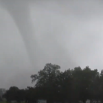 Tornado forming in the sky over a rural landscape, indicating severe weather conditions.