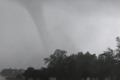 Tornado forming in the sky over a rural landscape, indicating severe weather conditions.