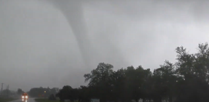 Tornado forming in the sky over a rural landscape, indicating severe weather conditions.