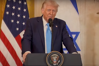 Donald Trump speaking at a podium with the U.S. and Israeli flags in the background.