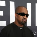 Kanye West at an event, wearing sunglasses and a black outfit.