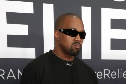 Kanye West at an event, wearing sunglasses and a black outfit.