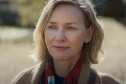 Naomi Watts smiling outdoors in a scarf, captured in a candid moment.