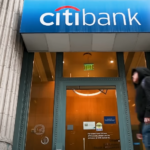 Citibank branch entrance with logo displayed above the glass doors, reflecting an urban street view.