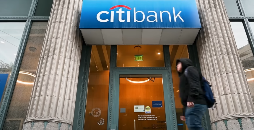 Citibank branch entrance with logo displayed above the glass doors, reflecting an urban street view.