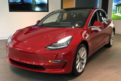 A red Tesla Model 3 on display at a showroom, representing the latest advancements, price changes, and autonomous driving technology in Tesla's 2025 lineup.