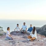 A group of people meditating together on a scenic hilltop during sunrise, embracing mindfulness and holistic wellness.