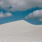 Snow-covered sand dunes under a cloudy sky, representing extreme weather conditions and shifting landscapes.