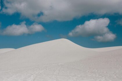 Snow-covered sand dunes under a cloudy sky, representing extreme weather conditions and shifting landscapes.