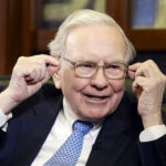 Warren Buffett wearing a suit and tie, smiling as he addresses attendees at the Berkshire Hathaway annual shareholders meeting.