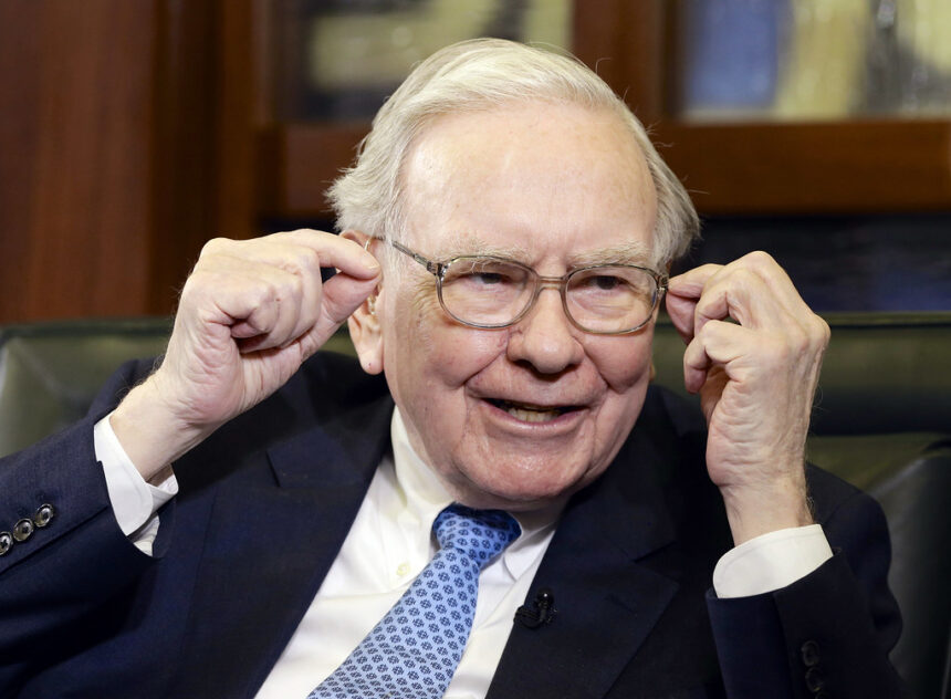 Warren Buffett wearing a suit and tie, smiling as he addresses attendees at the Berkshire Hathaway annual shareholders meeting.